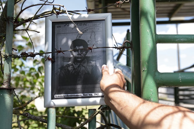 A man places a picture of a Roma victim of the Holocaust on the fence of the pig farm at the Lety concentration camp site. (REUTERS/David W Cerny)